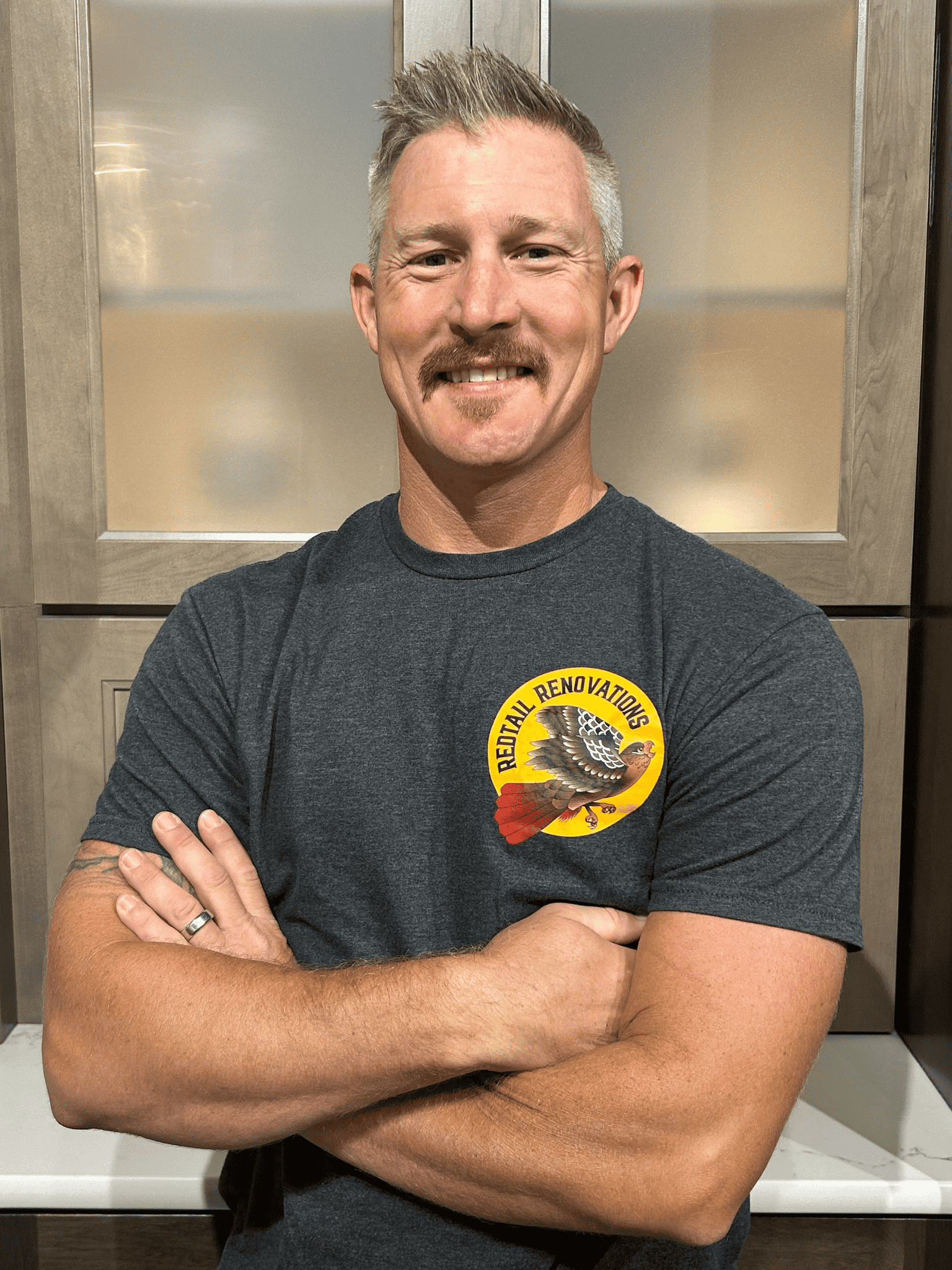 Smiling man with crossed arms wearing a gray T-shirt with a Federal Renovators logo.