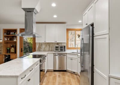 Bright modern kitchen with white cabinets, stainless steel appliances, and wooden flooring.
