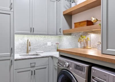 Contemporary laundry room with gray cabinets, wooden shelves, and a washing machine.