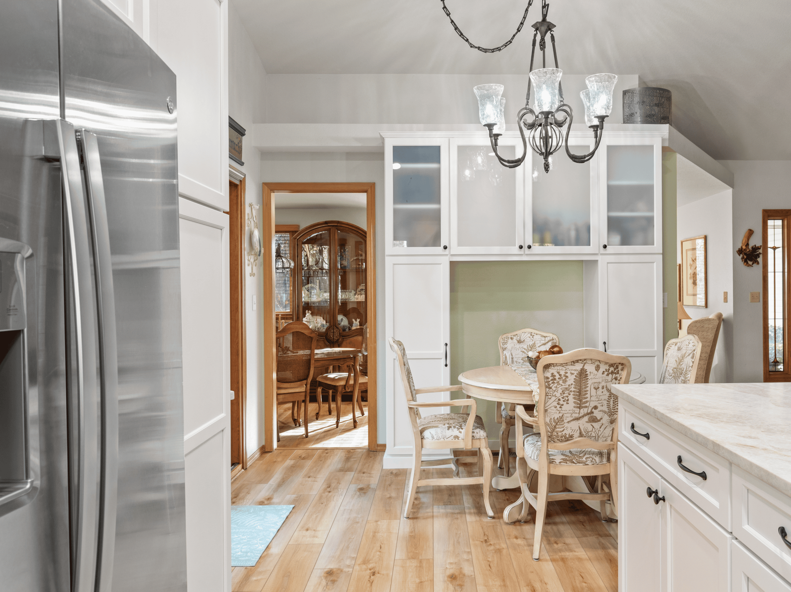 Example Co Kitchen Bright kitchen with white cabinets, chandelier, and dining area with vintage chairs.