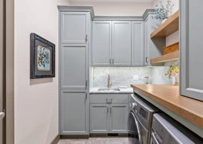 Light gray kitchen cabinets with wooden shelves and a washer and dryer.