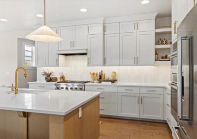 Bright white kitchen with gold accents, island, and stainless steel appliances.