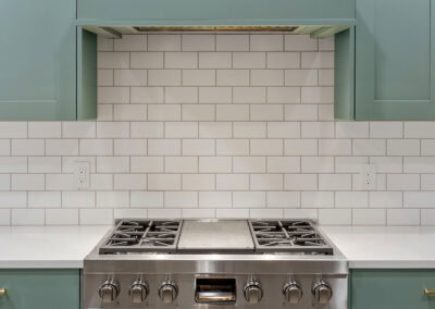 Contemporary kitchen with teal cabinets, white subway tile backsplash, and stainless steel stove.