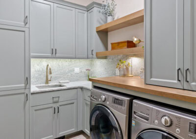 Contemporary laundry room with light gray cabinets and wooden shelves.
