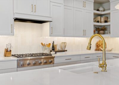 Bright modern kitchen with white cabinets, gold fixtures, and a sleek countertop.