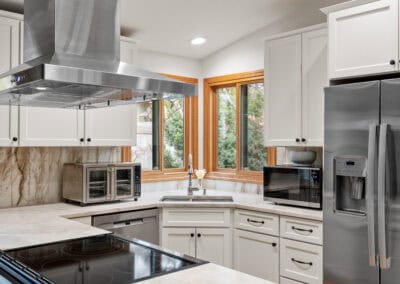 Bright modern kitchen with white cabinets, stainless steel appliances, and large windows.
