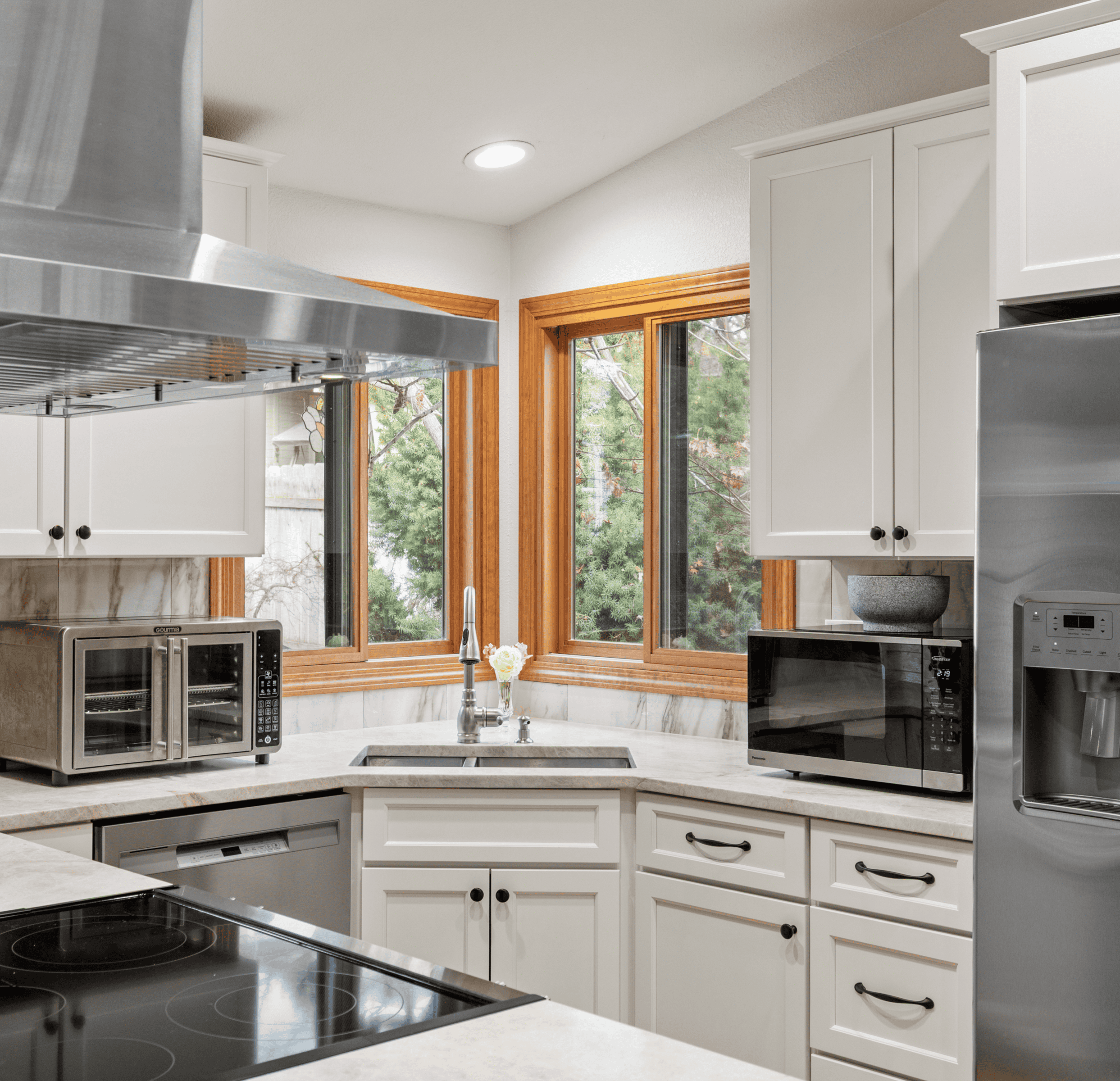 Modern Kitchen Design Bright modern kitchen with white cabinets, marble countertops, and large windows overlooking theyard.
