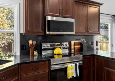 Kitchen with dark wood cabinets, stainless steel stove, microwave, and black granite countertops.
